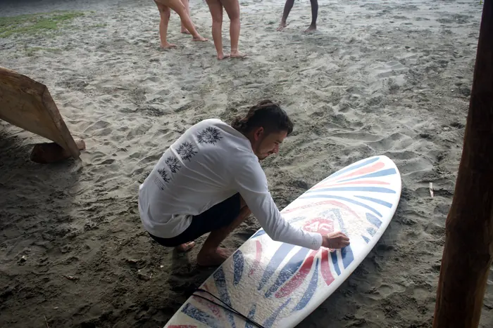 Instructor encerando una tabla de surf en la arena