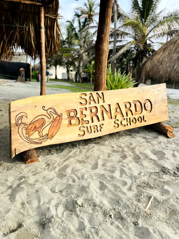 Letrero tallado en madera de San Bernardo Surf School sobre la arena
