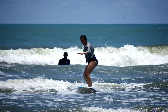 Alumna equilibrándose sobre la tabla con el instructor detrás en el agua