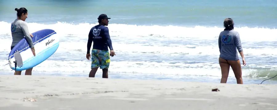 Alumnas e instructor caminando hacia el mar con una tabla